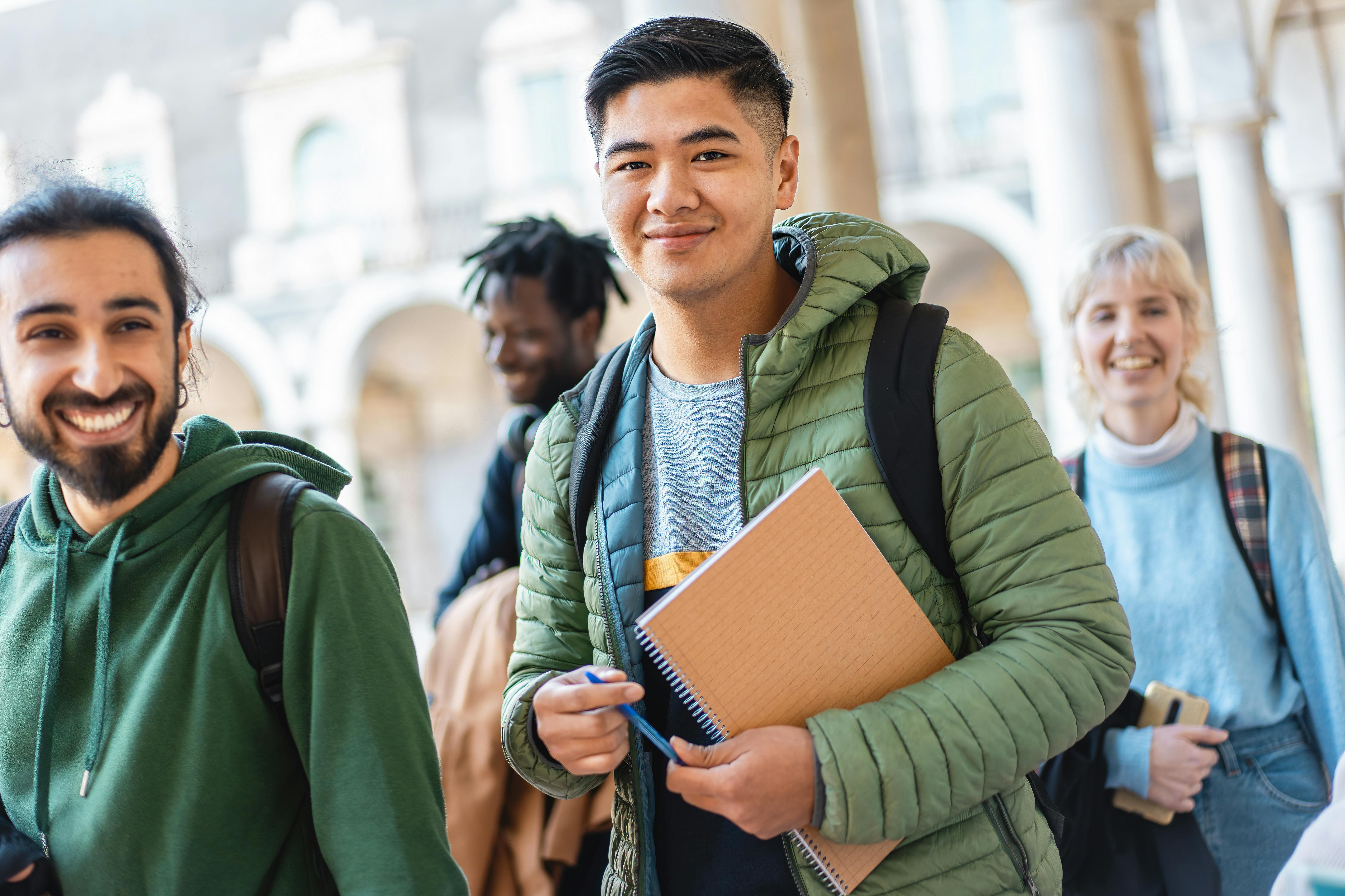 Iloiset opiskelijat kirjojen ja reppujen kanssa jakavat iloisen hetken, ilmentäen ystävyyttä ja monimuotoisuutta.