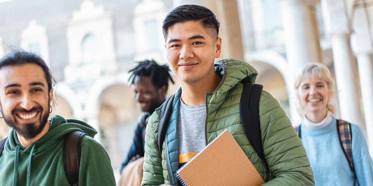 Iloiset opiskelijat kirjojen ja reppujen kanssa jakavat iloisen hetken, ilmentäen ystävyyttä ja monimuotoisuutta.